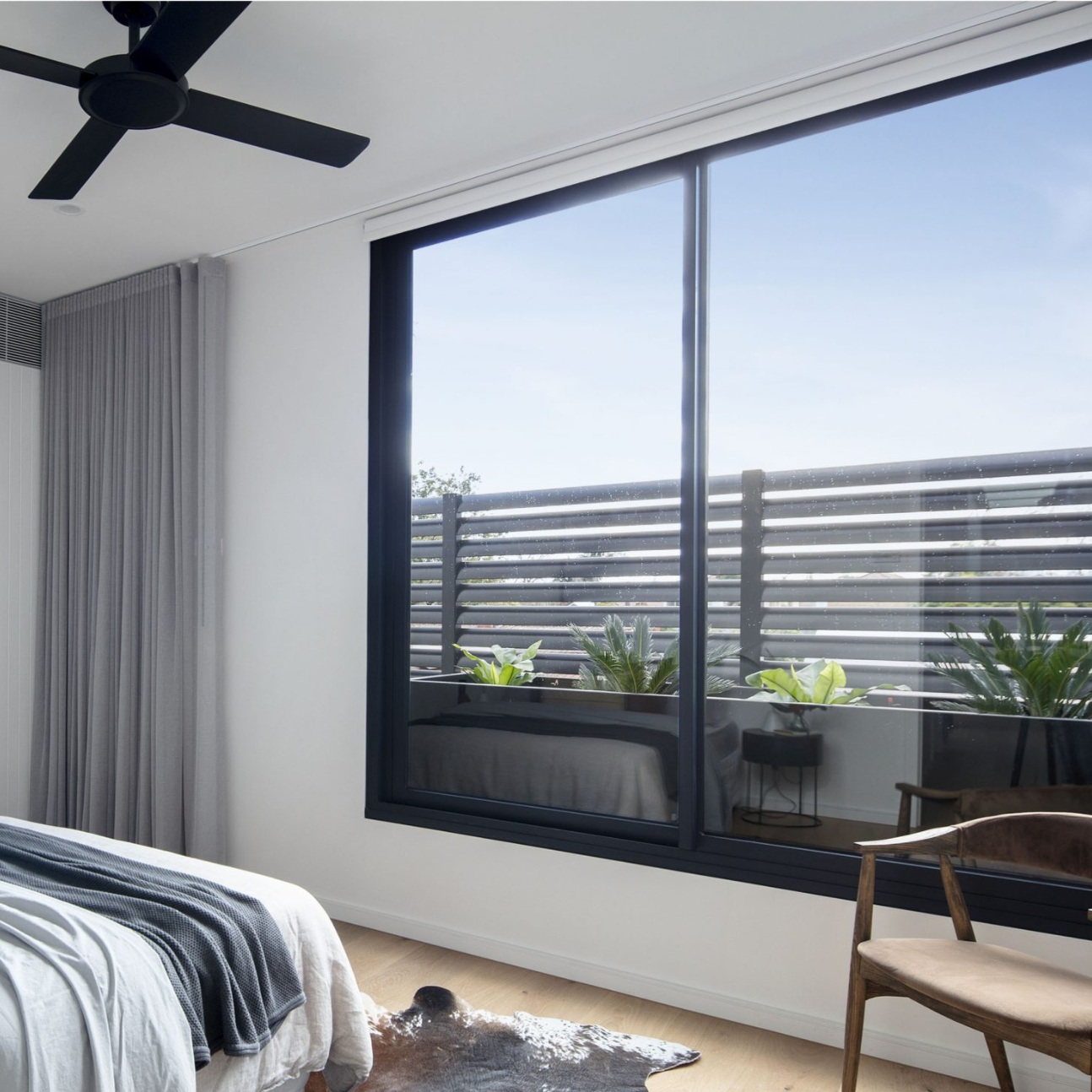 Modern bedroom with large aluminium sliding window, bed, and chair.