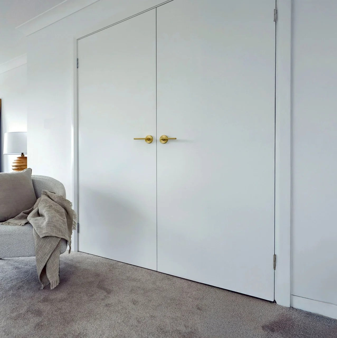 White Shield Doors & Windows flush hollowcore internal door with gold handles in a room with a gray sofa and lamp.